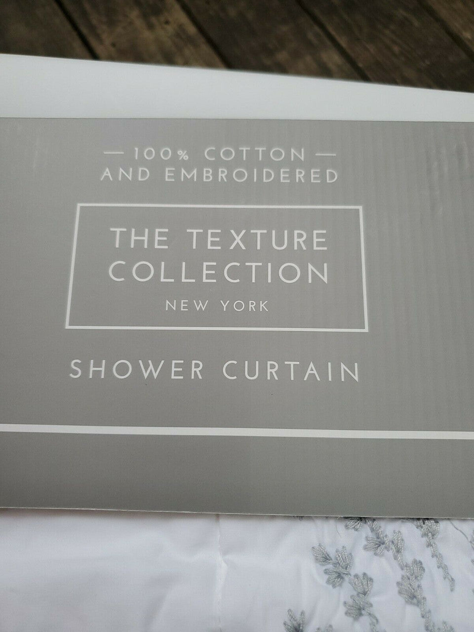 Folded white 100% cotton embroidered shower curtain from The Texture Collection shown in retail packaging