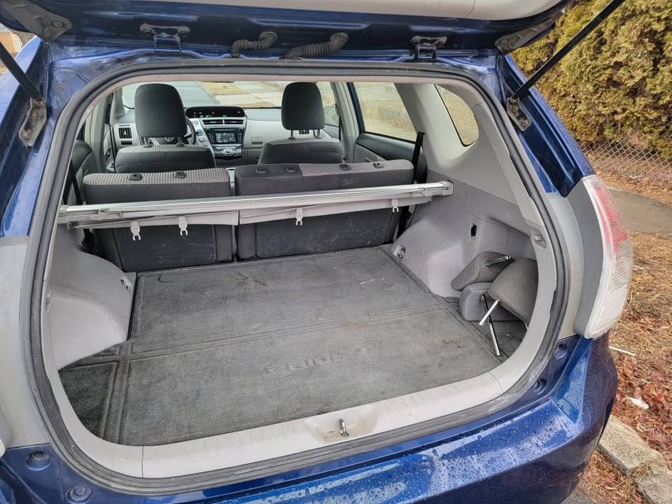 Rear cargo area of a 2015 Toyota Prius v with hatch open, showing spacious trunk space, folded privacy cover, and back of rear seats