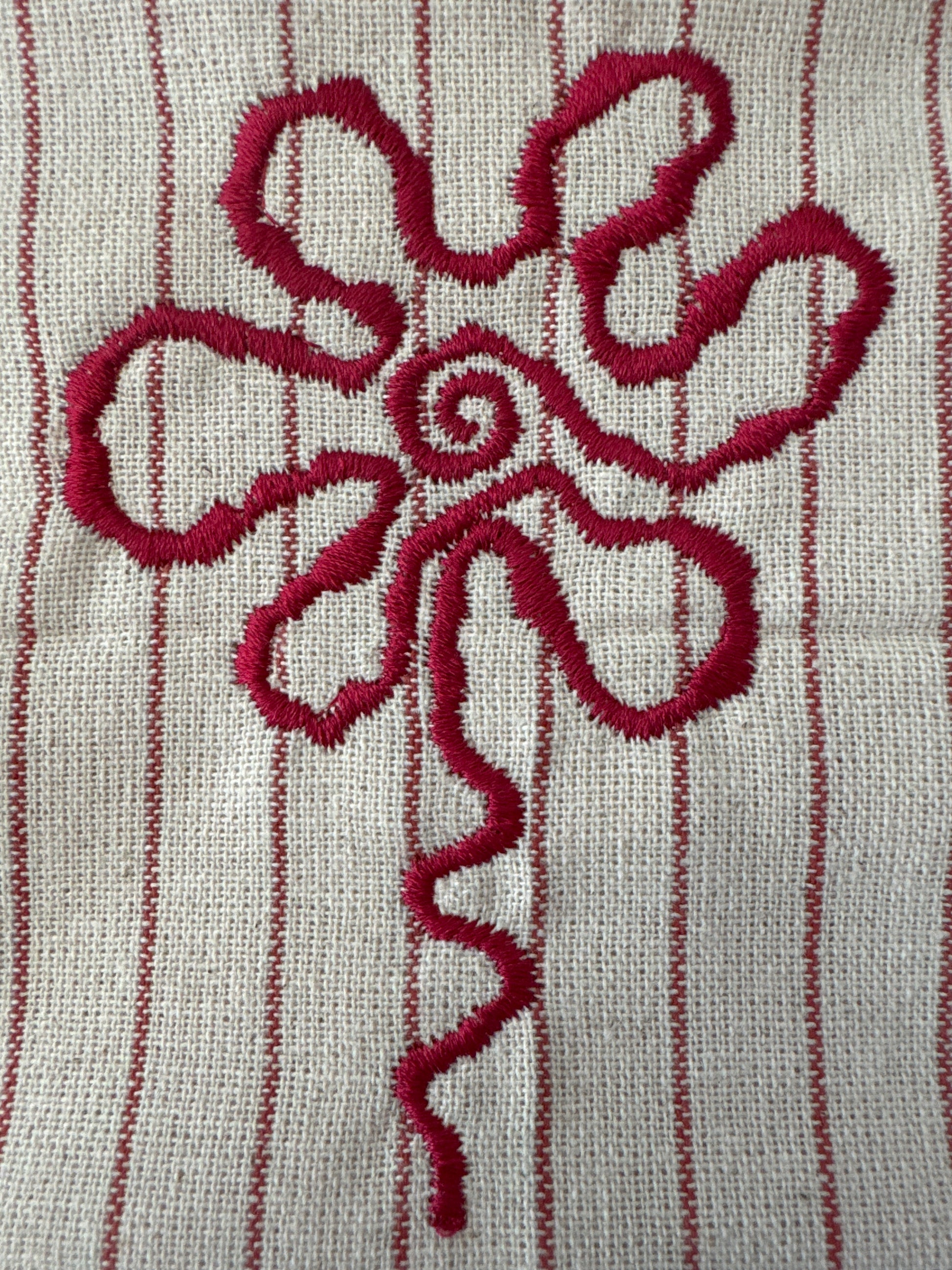 Close-up of beige fabric with red vertical stripes featuring an embroidered red flower-like design with a spiral center and flowing petal-like shapes